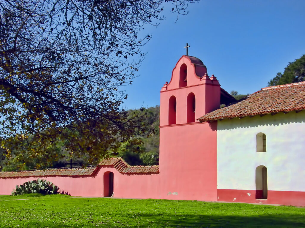 Restored pink-red mission bell wall and adobe buildings at La Purísima Mission State Historic Park in Lompoc, California