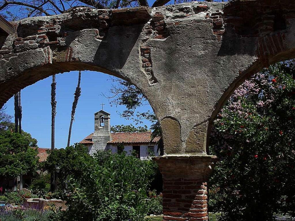 Stone arcade ruins framing buildings and gardens at Mission San Juan Capistrano, California