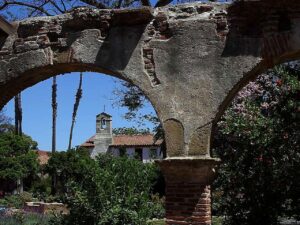 Stone arcade ruins framing buildings and gardens at Mission San Juan Capistrano, California