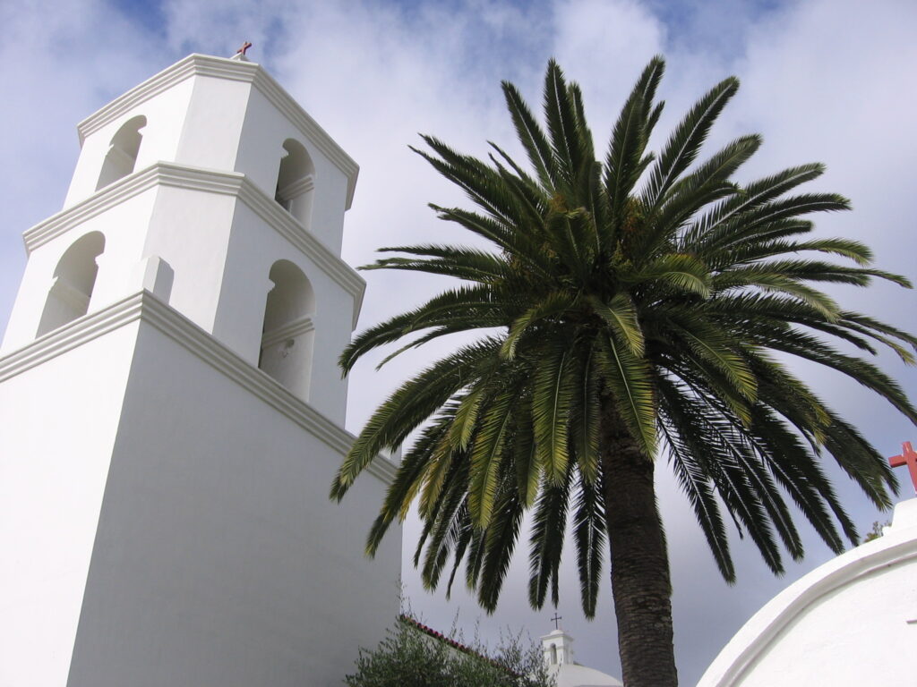 Historic white Mission San Luis Rey church and a tall palm tree in Oceanside, California