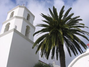 Historic white Mission San Luis Rey church and a tall palm tree in Oceanside, California