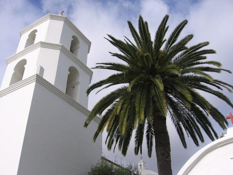 Historic white Mission San Luis Rey church and a tall palm tree in Oceanside, California