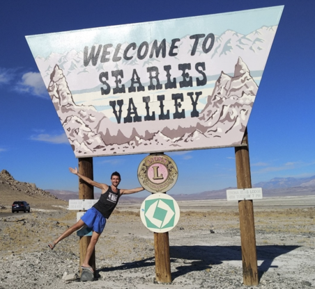 Welcome to Searles Valley roadside sign in the California desert with a visitor posing beside it